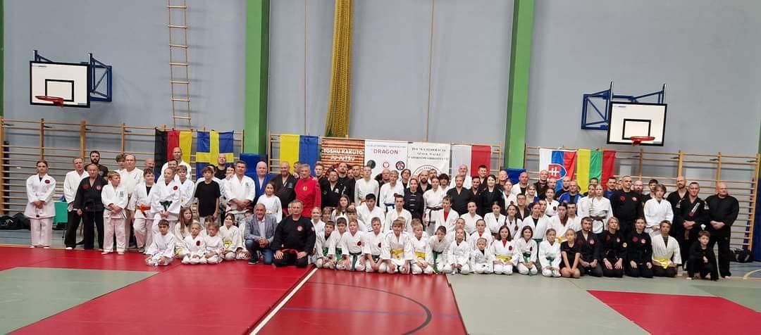 Duże grupowe zdjęcie uczestników wydarzenia RAIMEI na hali sportowej.